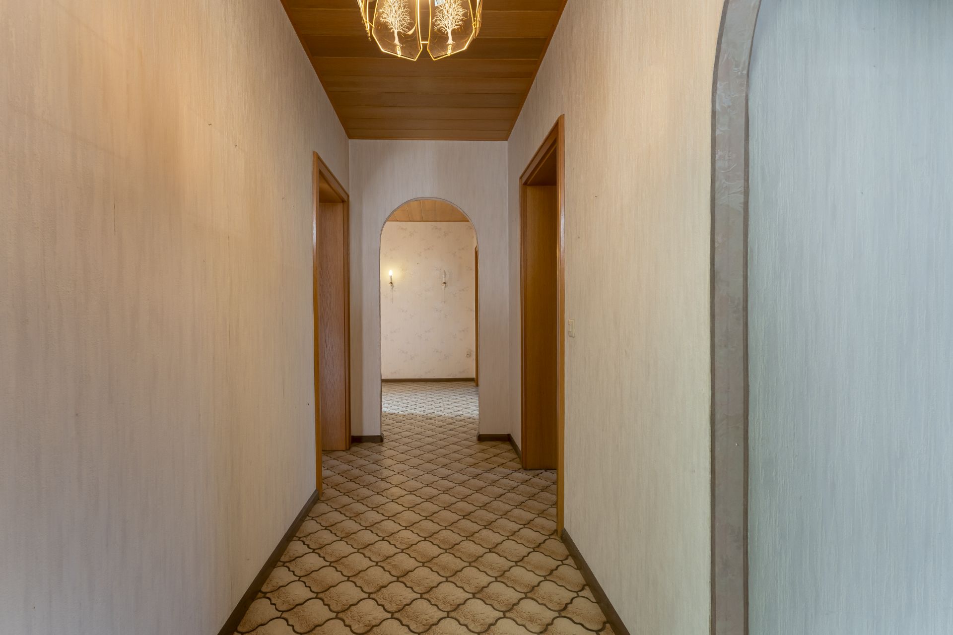Langer Flur mit Teppichboden, Holztüren und einer Deckenlampe in einem Wohnhaus.