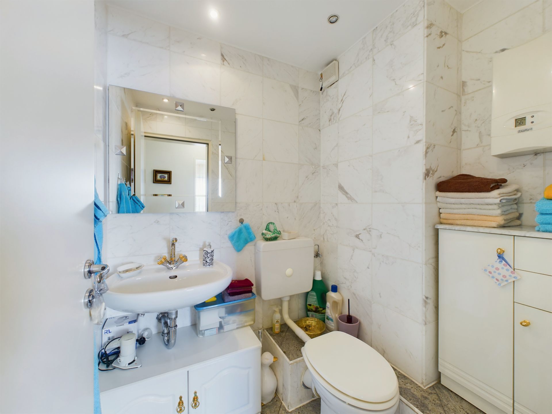 Kleines Badezimmer mit WC, Waschbecken, Spiegel und Schränken, weiß gekachelte Wände.