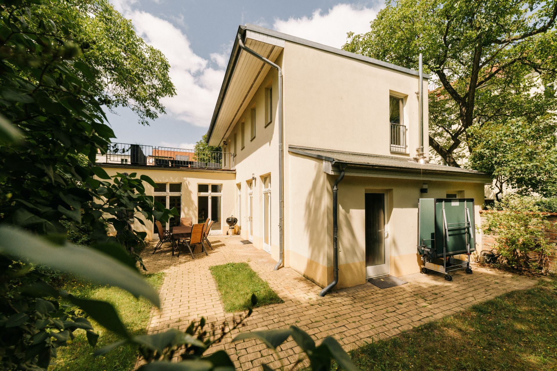 Zweistöckiges Wohnhaus mit Terrasse, Gartenmöbeln und umgeben von Bäumen.