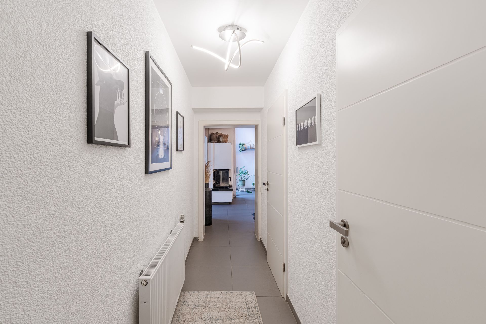 Heller Flur mit weißen Wänden, Wandbildern, Heizkörper und moderner Deckenleuchte.
