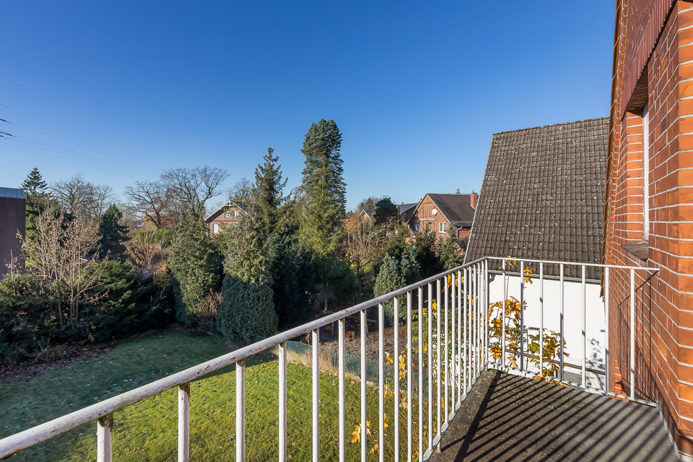 Blick von einem Balkon auf einen Garten mit Bäumen und Nachbarhäusern bei klarem Himmel.