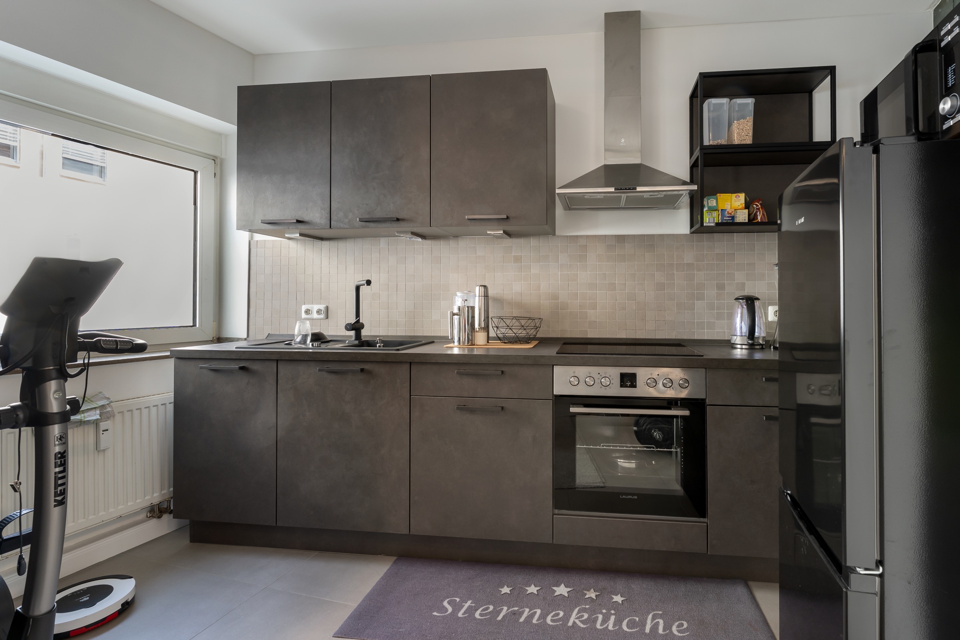 Moderne Küche mit grauen Schränken, Elektroherd, Ofen und großer Kühlschrank.