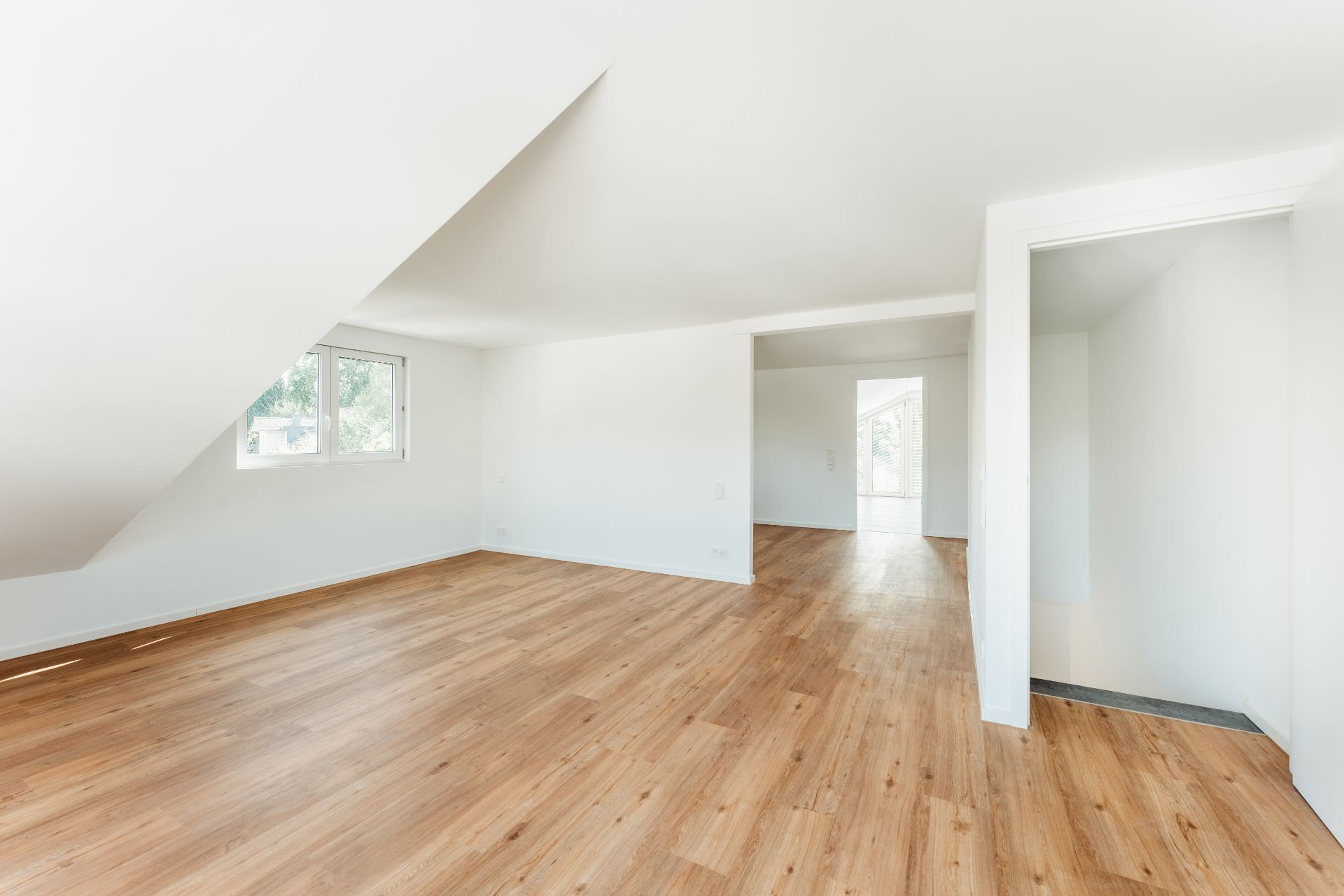 Heller Raum mit schräger Decke, Holzfußboden und weiß gestrichenen Wänden.