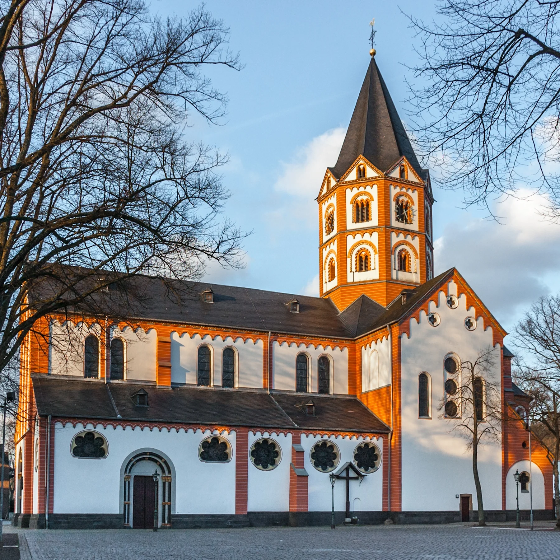 Stadtpanorama mit Kirche, historischen Gebäuden und Schiffen am Flussufer bei sonnigem Wetter.