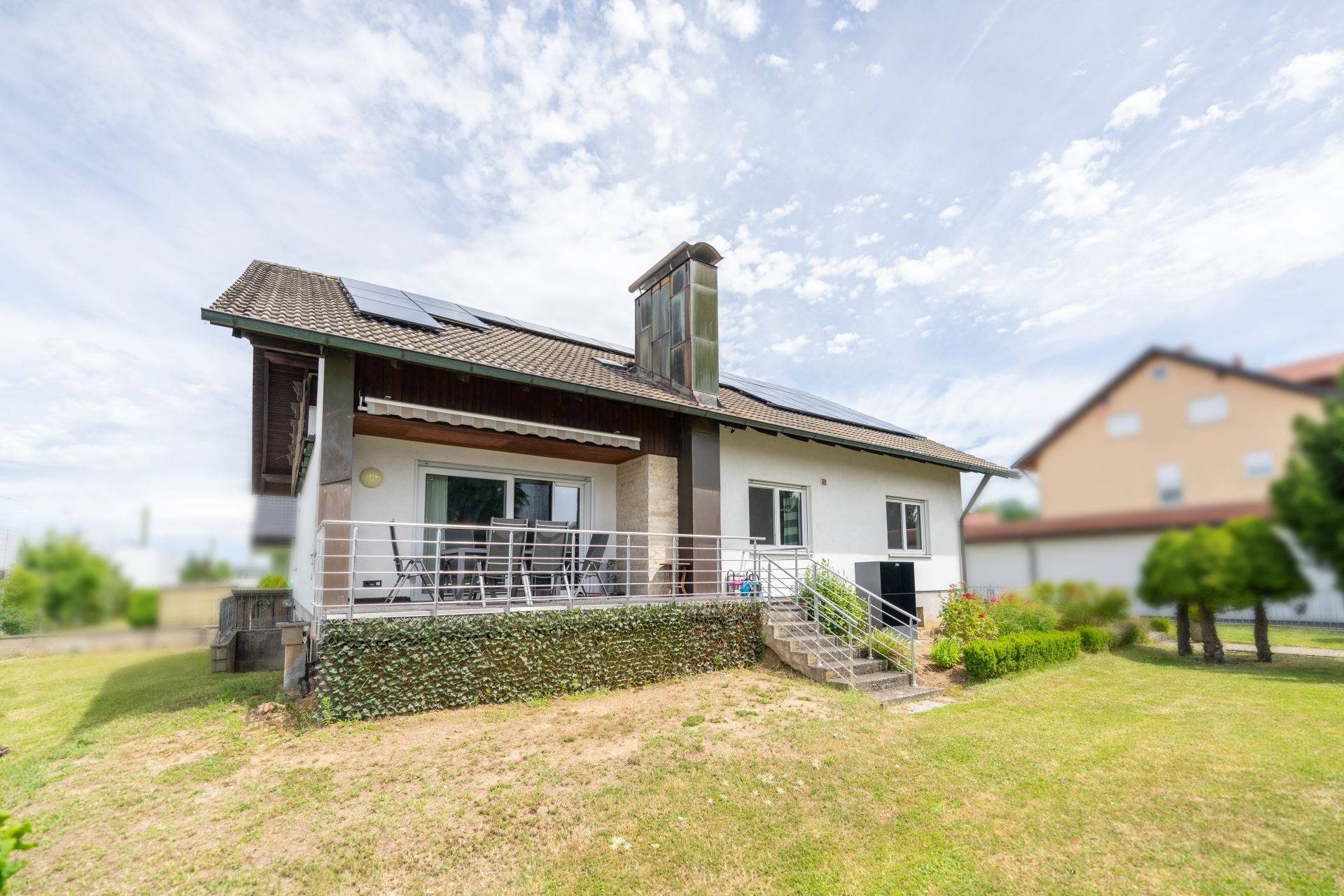Einfamilienhaus mit Terrasse, Garten und Solarpanelen auf dem Dach.