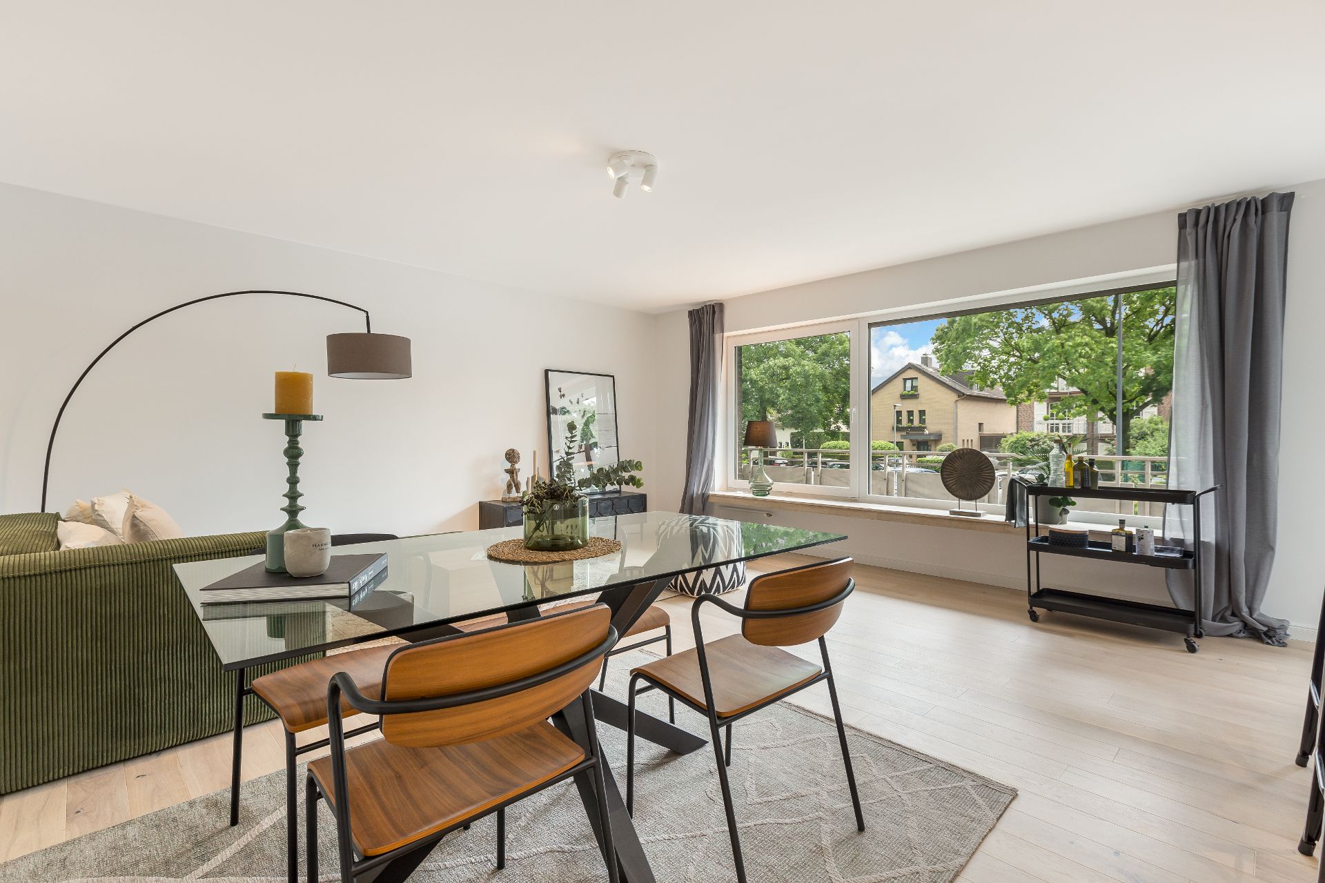 Helles Wohnzimmer mit Glastisch, Holzstühlen und großem Fenster mit Blick ins Grüne.