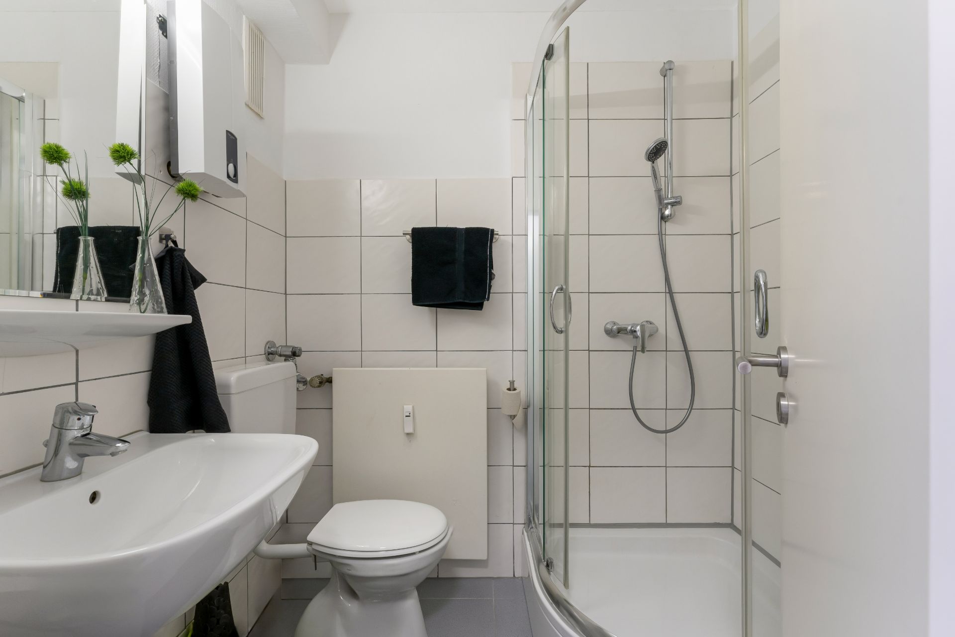 Modernes Badezimmer mit Dusche, Waschbecken, WC und Spiegel, helle Fliesen an den Wänden.