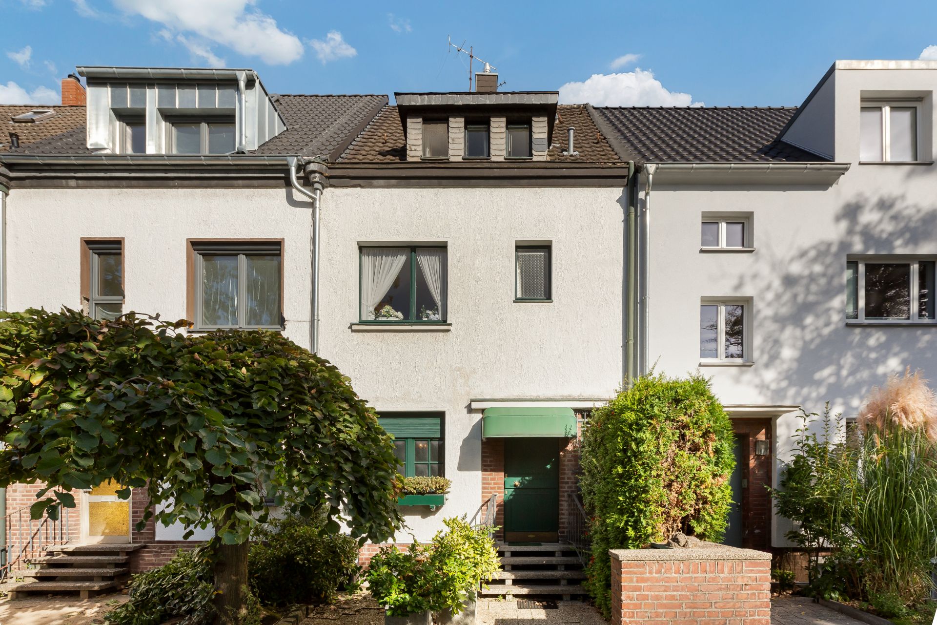 Vorderansicht eines weißen Reihenhauses mit grünem Eingang und Garten.