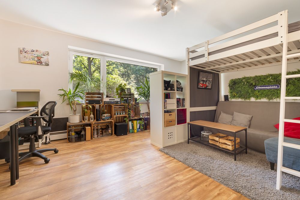 Helles Wohn- und Arbeitszimmer mit Hochbett, Sofa, Schreibtisch, großen Fenstern und vielen Pflanzen.
