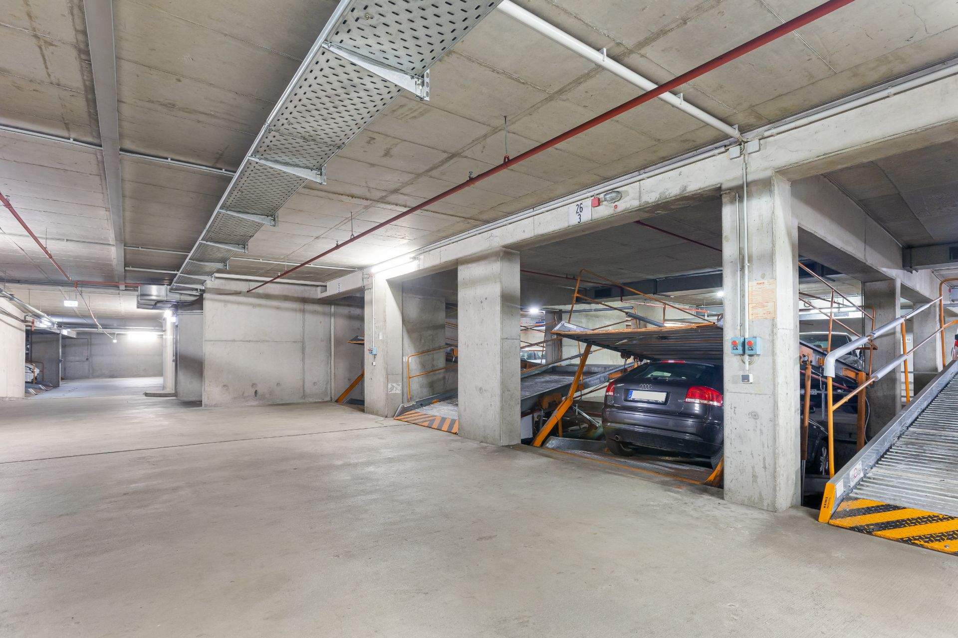 Tiefgaragenstellplätze mit Betonwänden, einem Auto und Rampen für weitere Fahrzeuge.