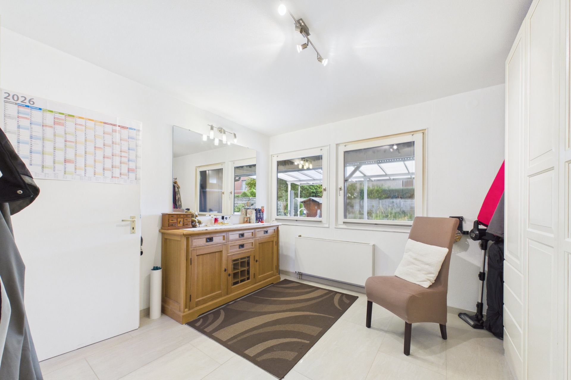 Helles Zimmer mit Spiegel, Holzkommode, Stuhl und Fenster mit Blick nach draußen.