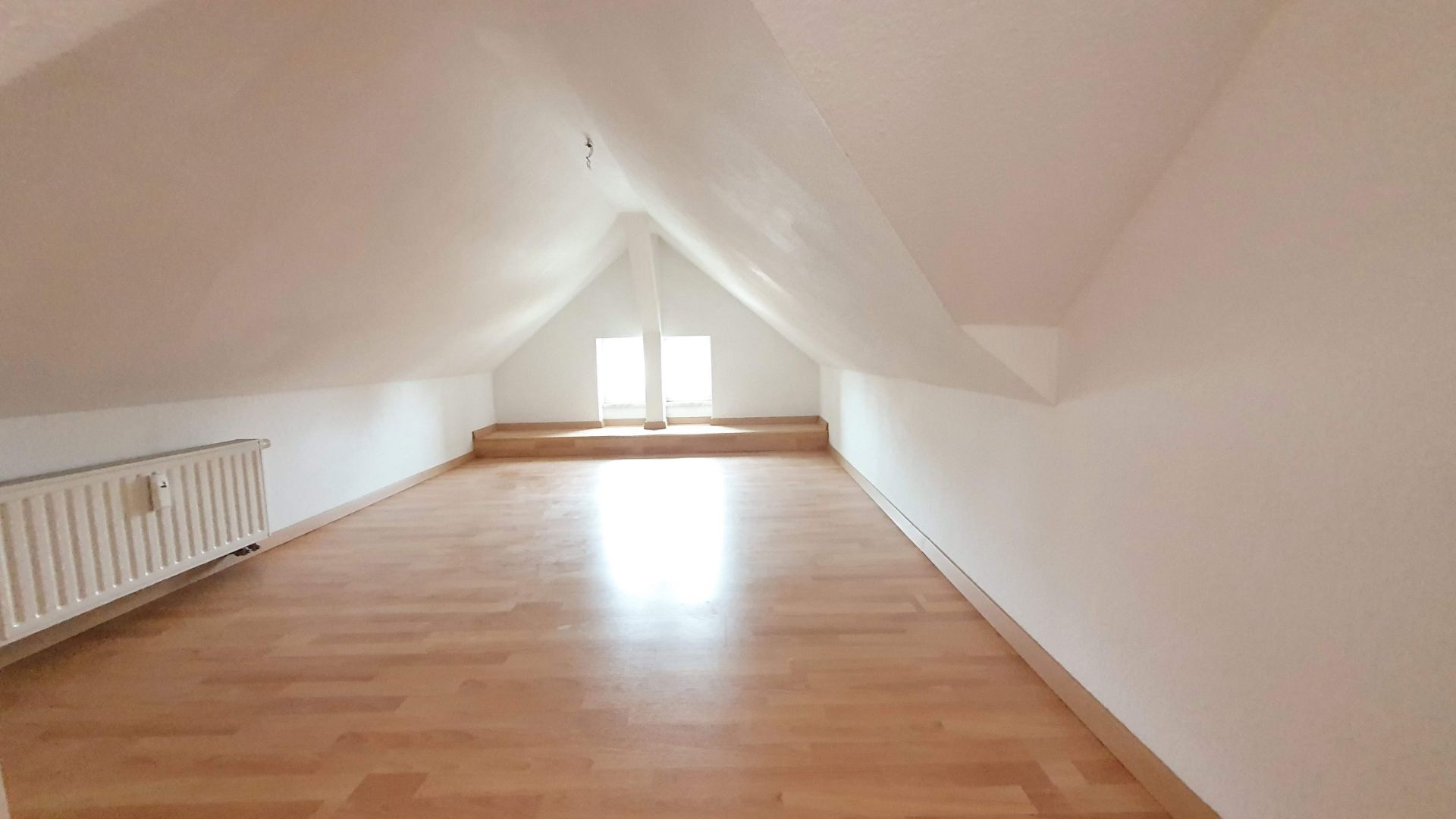 Heller Dachbodenraum mit Holzfußboden, weiß gestrichenen Wänden und zwei kleinen Fenstern.