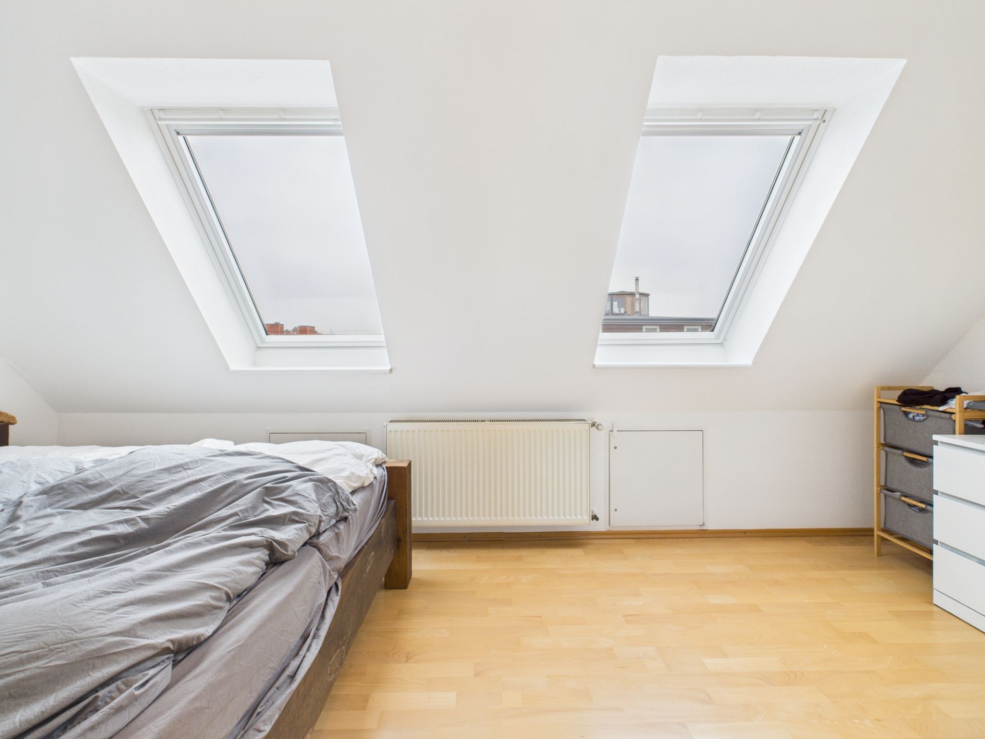 Helles Schlafzimmer mit zwei Dachfenstern, Holzboden, Bett und Kommode.