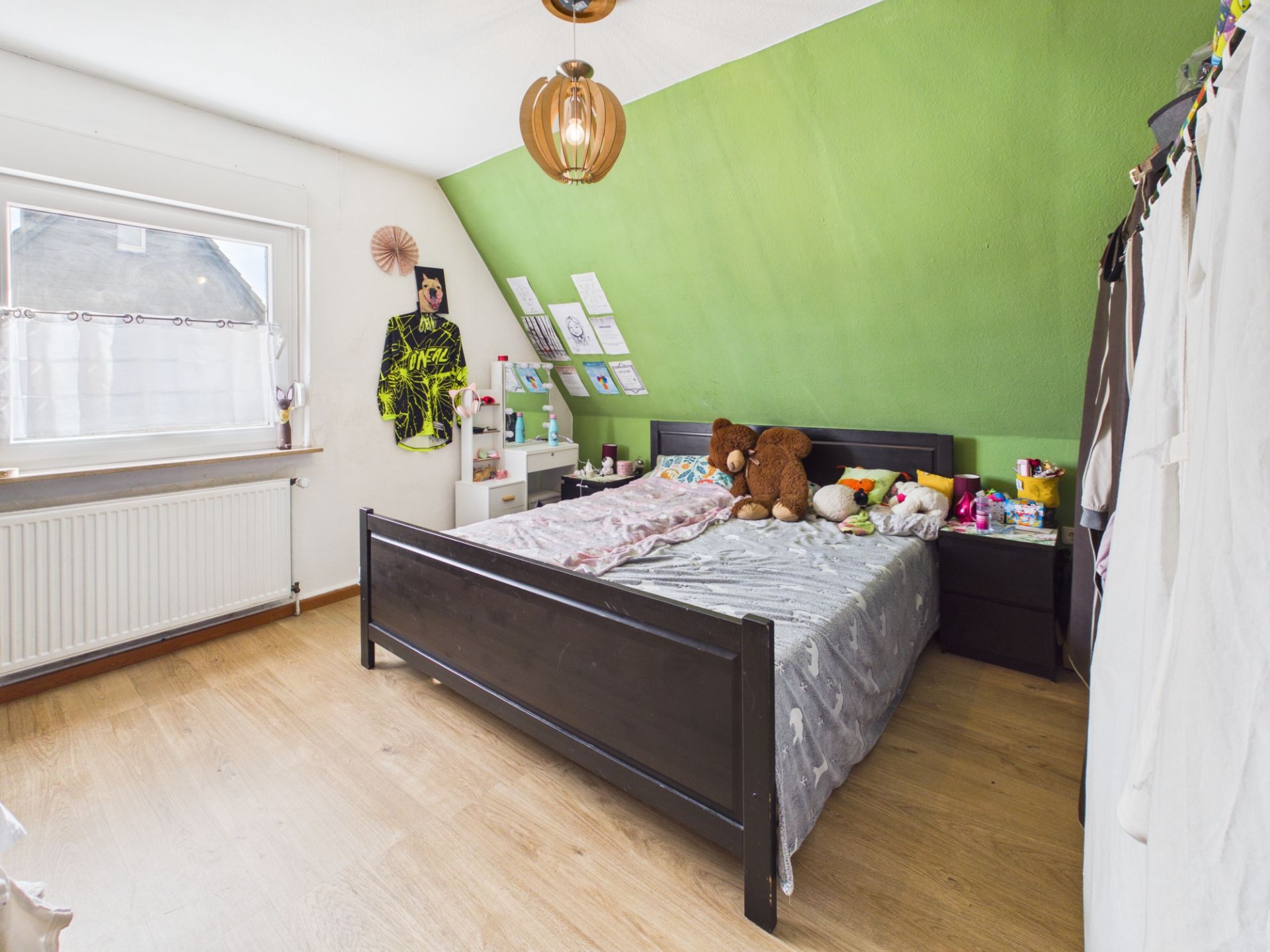 Schlafzimmer mit grün gestrichener Wand, Doppelbett, Plüschtieren und Fenster.