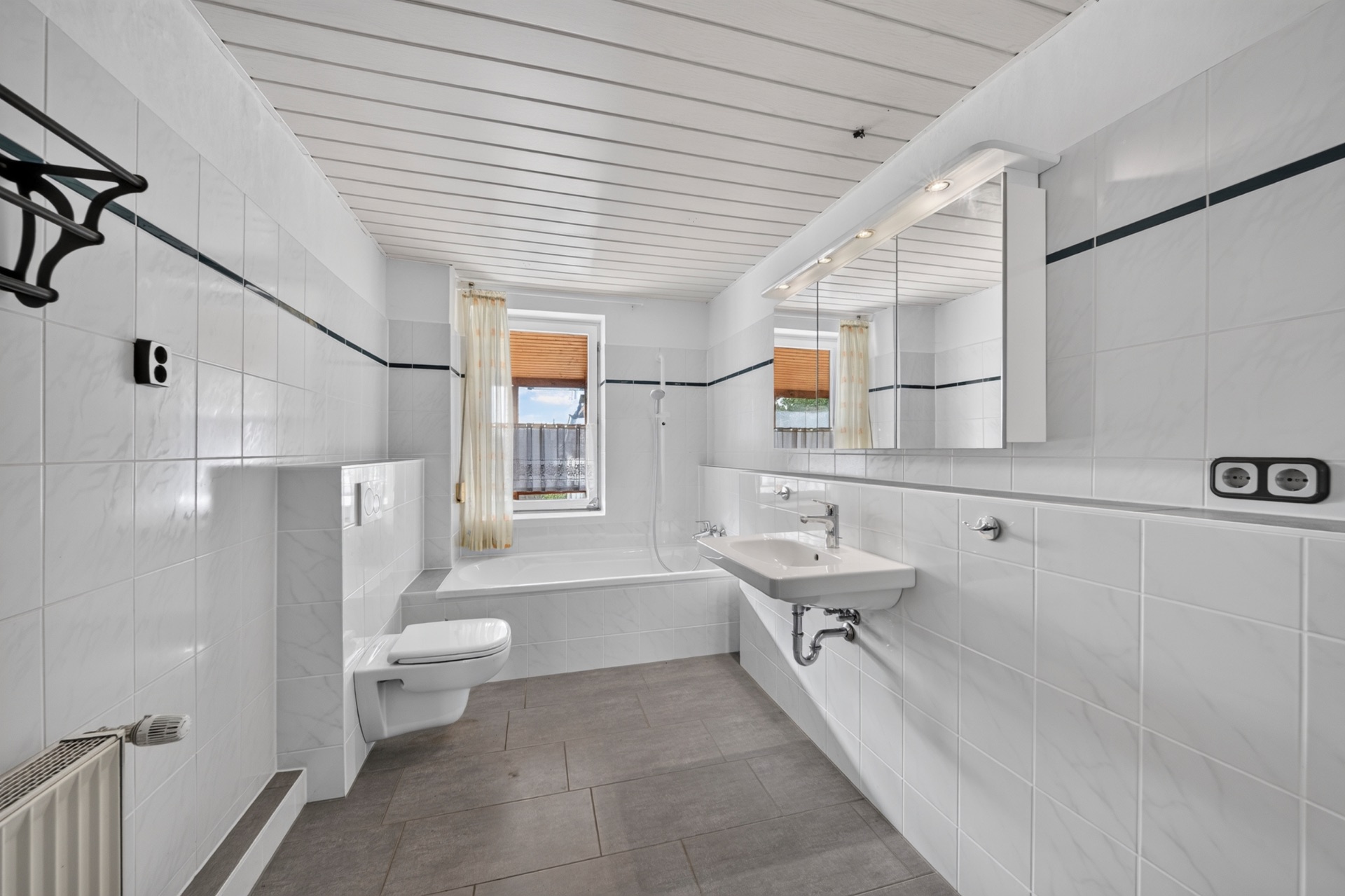 Helles Badezimmer mit Badewanne, Wandtoilette, Waschbecken und großem Spiegel.