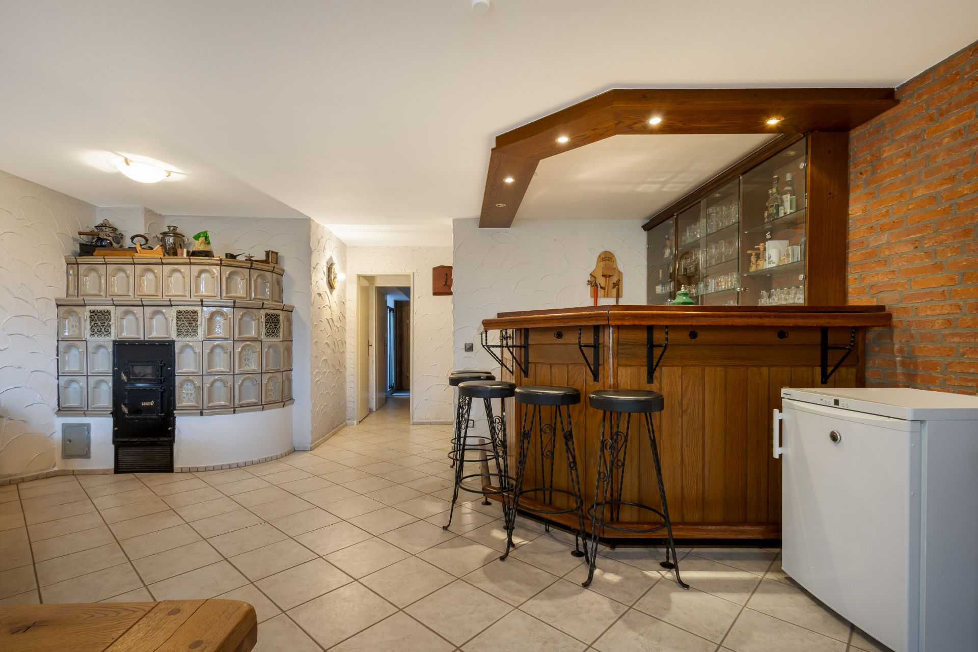 Wohnzimmer mit Bartresen, Hockern, Kaminofen und Fliesenboden.