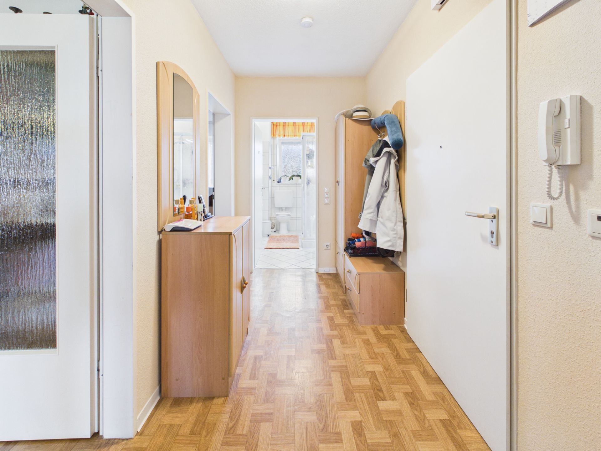 Heller Flur mit Holzkommode, Spiegel, Garderobe und Blick ins Badezimmer.