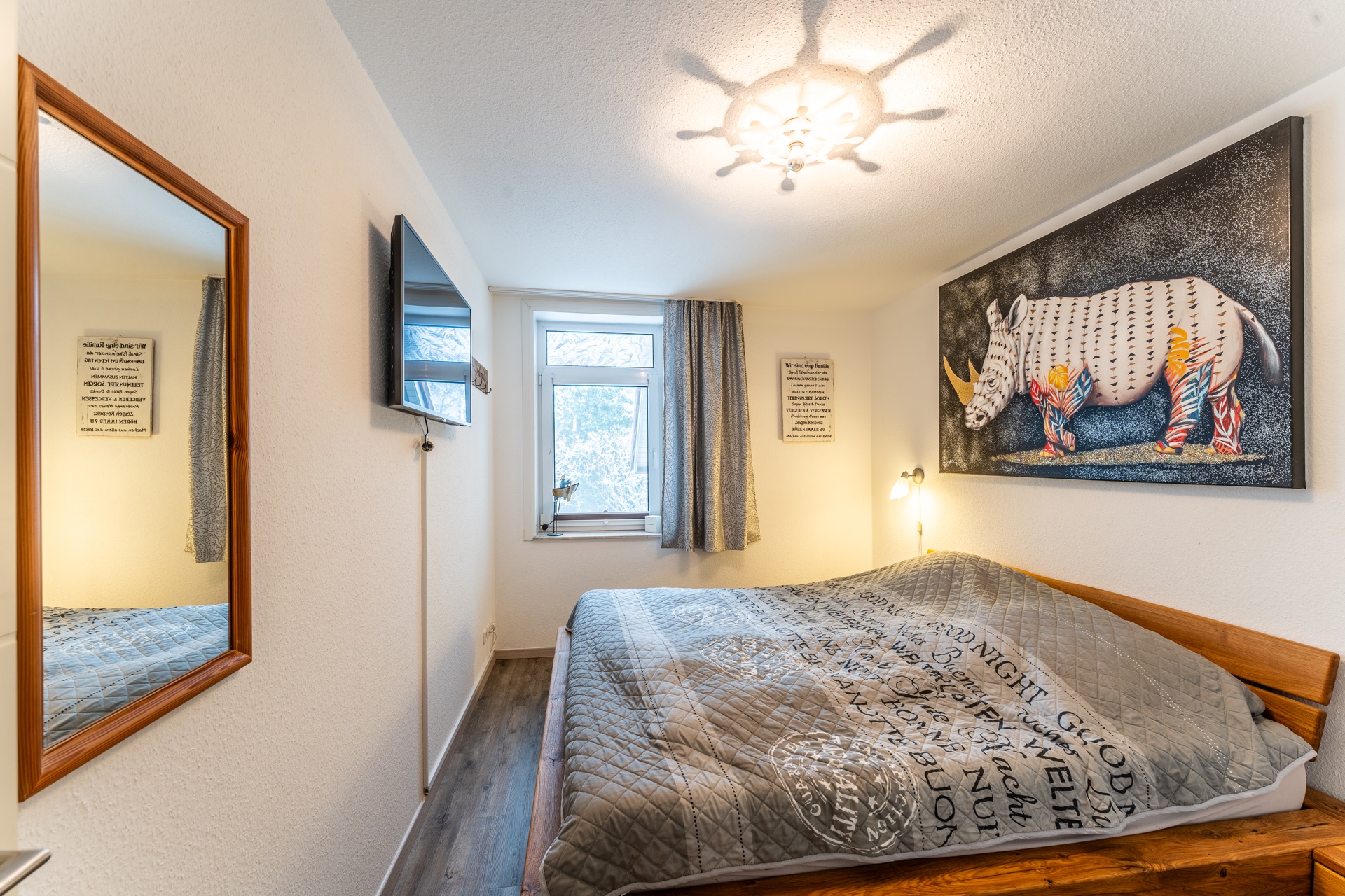Schlafzimmer mit Doppelbett, Wandbild eines Nashorns, Fenster, Spiegel und Fernseher an der Wand.