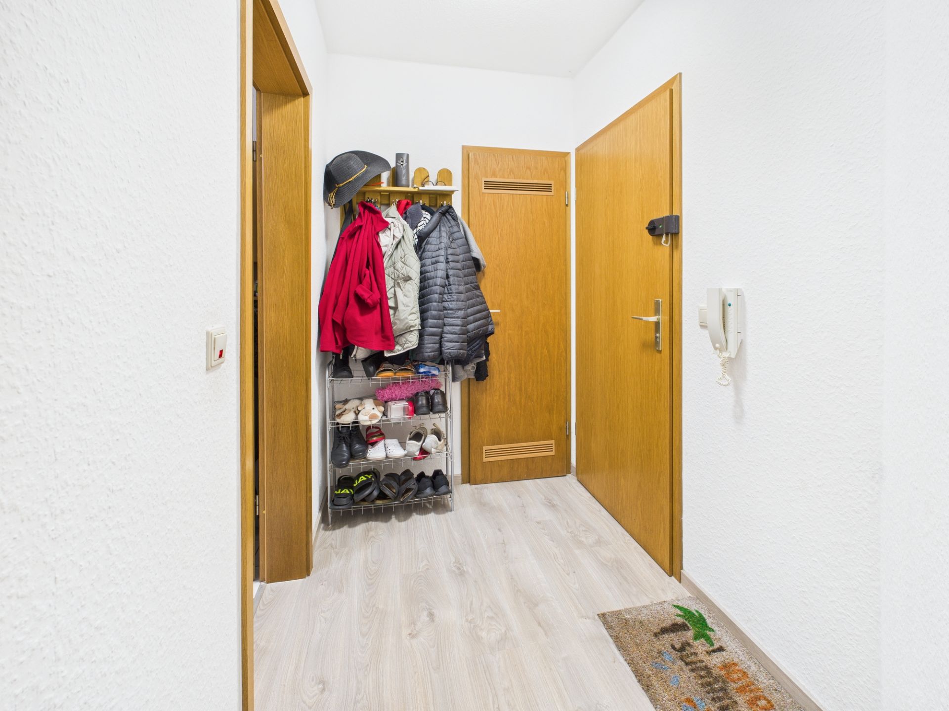 Flur mit Garderobe, Jacken, Schuhregal, Holztüren und hellem Boden.