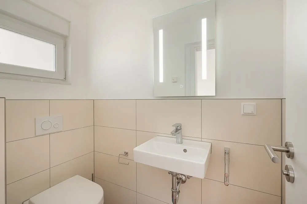 Modernes kleines Bad mit Waschbecken, Spiegel, Toilette und Fenster.