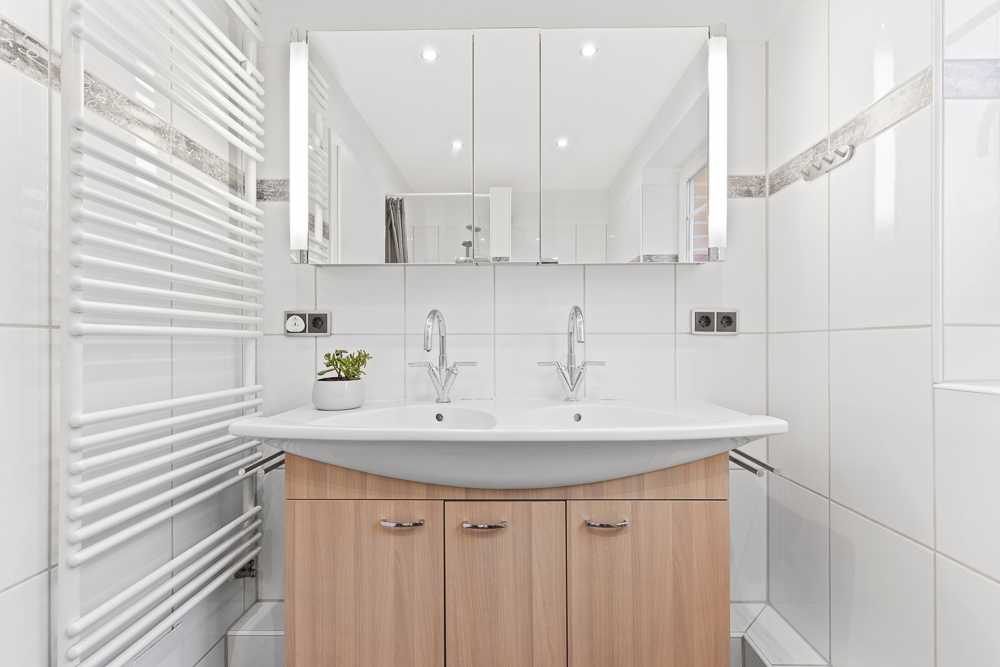 Modernes Badezimmer mit Doppelwaschbecken, Holzunterschrank, Spiegel und weißem Handtuchheizkörper.