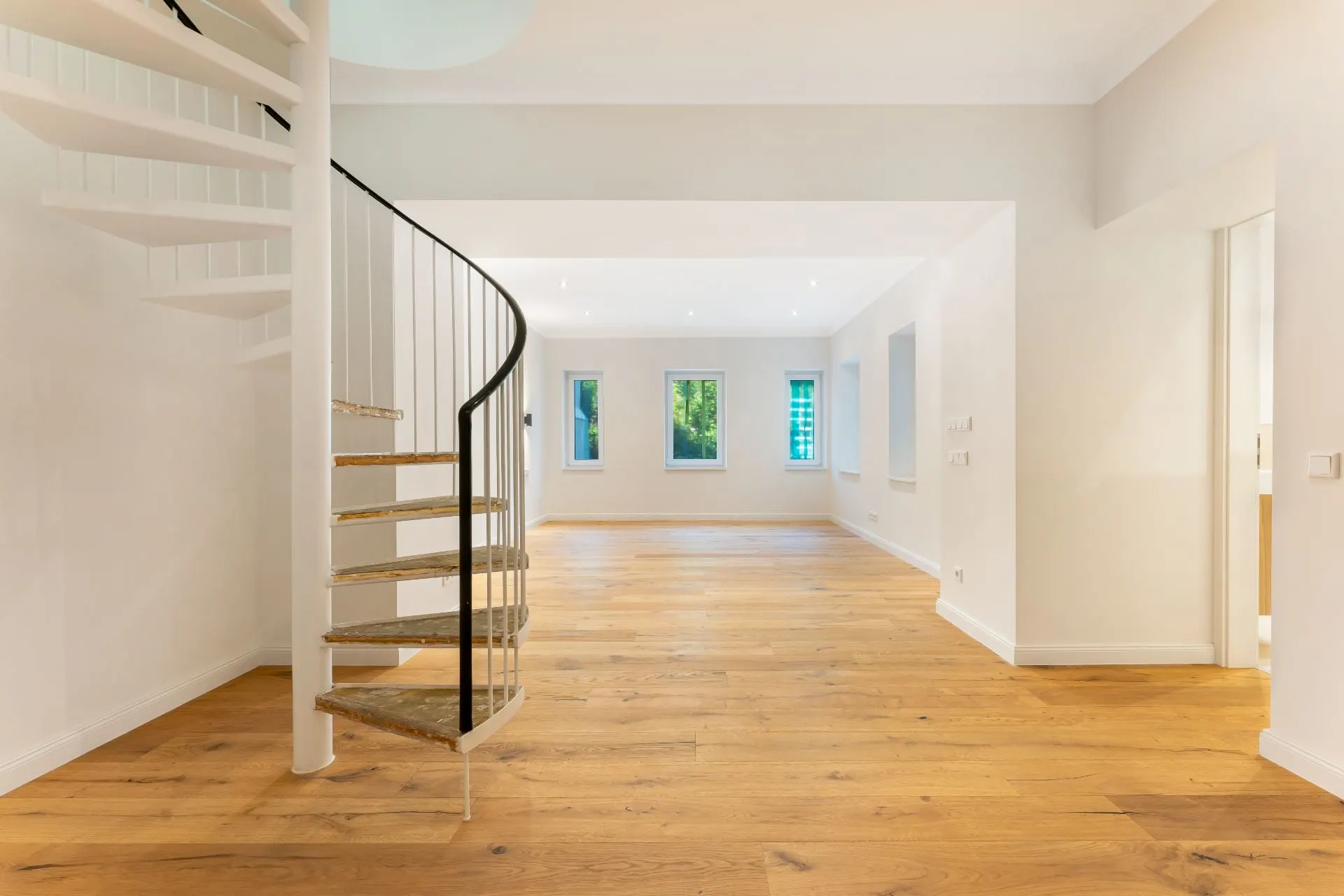 Heller Raum mit Holzfußboden, weißen Wänden und einer weißen Wendeltreppe.