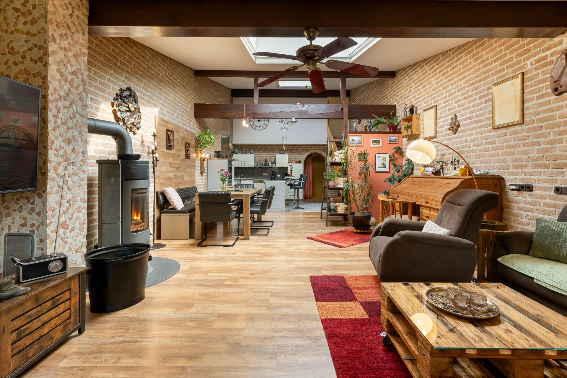 Offenes Wohnzimmer mit Kaminofen, Holzmöbeln und Blick auf Essbereich und Küche.