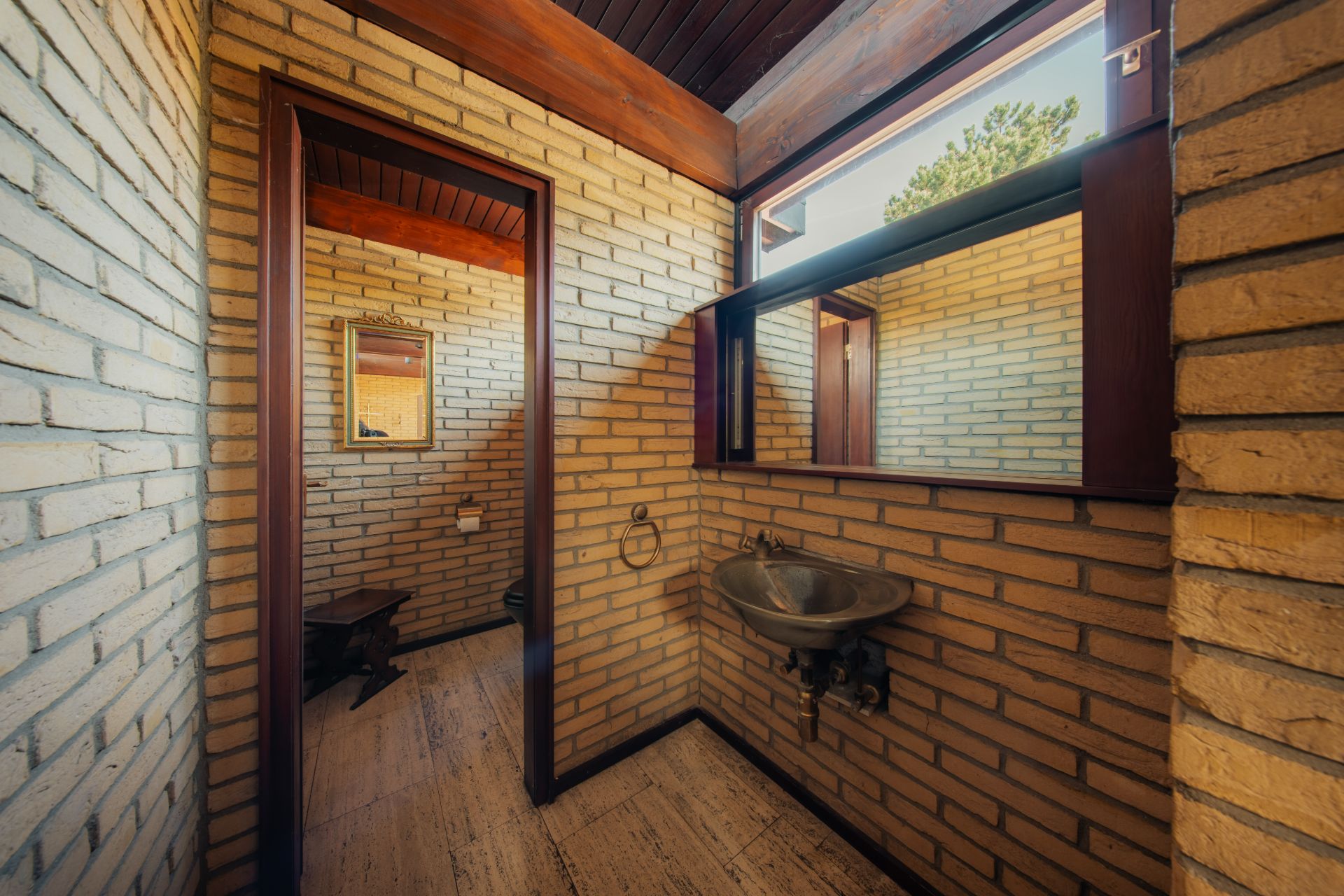 Badezimmer mit Waschbecken, großem Spiegel und WC, Wände aus gelben Ziegelsteinen.