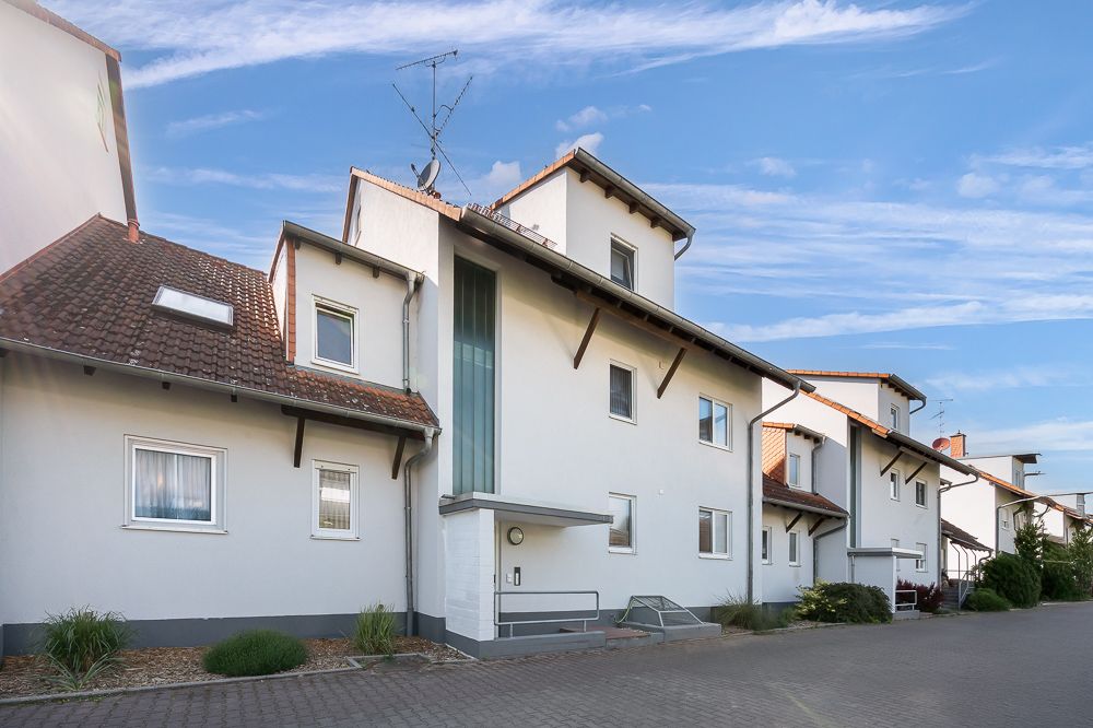 Mehrfamilienhaus mit weißen Fassaden, roten Dächern und großen Fenstern an einer ruhigen Straße.