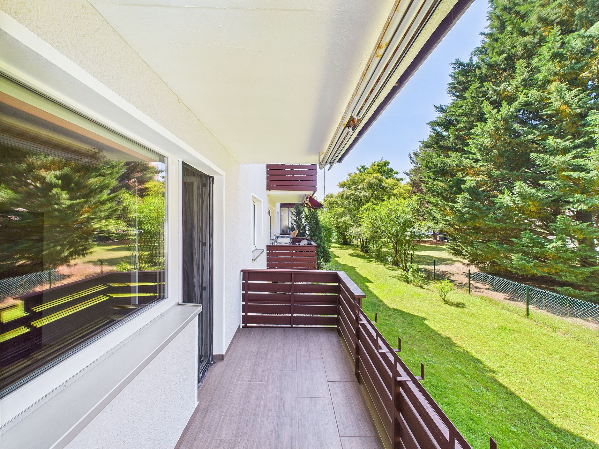 Langer Balkon mit Holzgeländer und Blick auf Garten mit Bäumen.