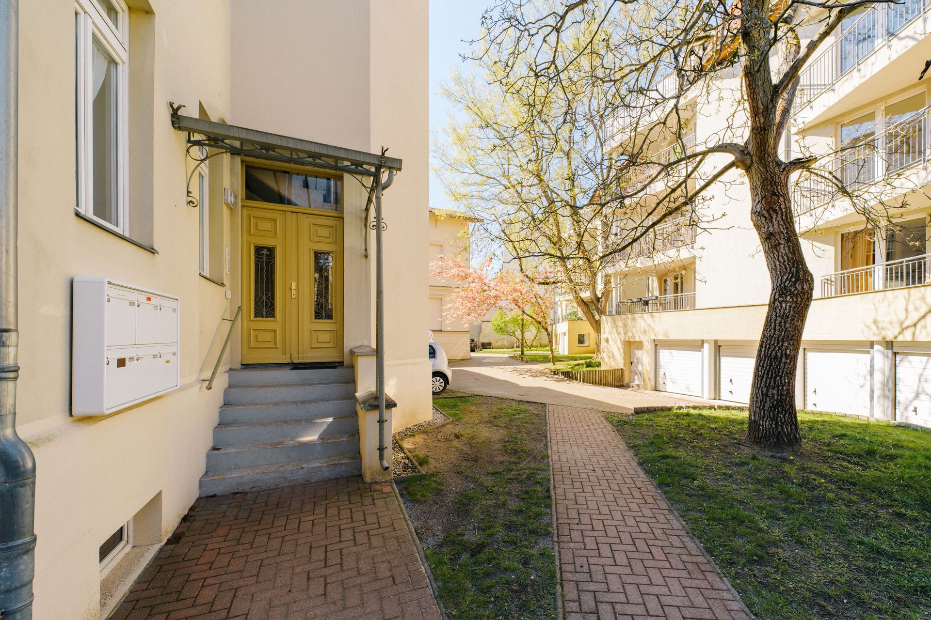 Eingang zu einem Wohnhaus mit gelber Tür, Treppe und Briefkästen an der Wand.