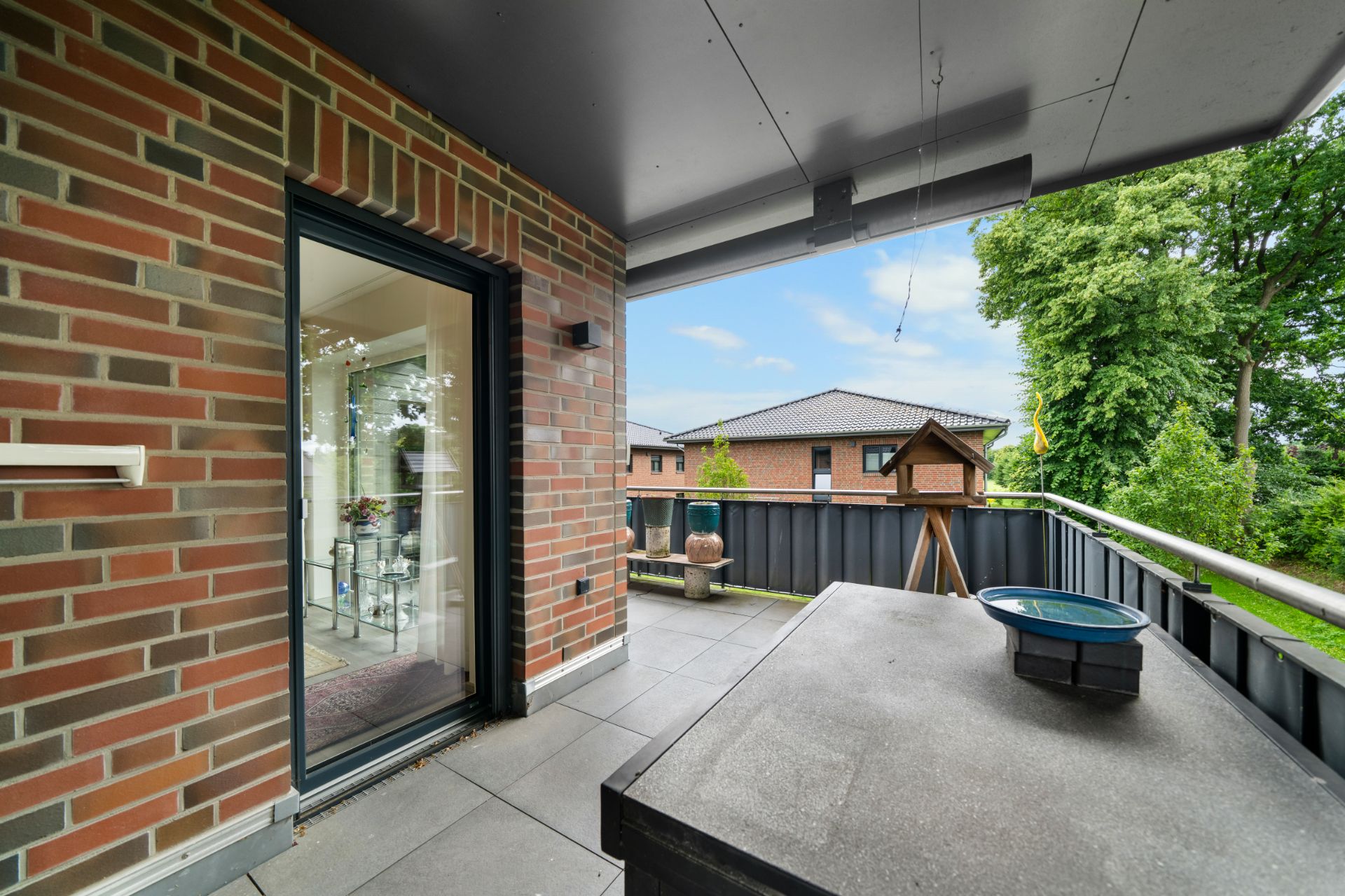 Überdachter Balkon mit Ziegelturm, Tisch und Blick auf Nachbarhäuser und Bäume.