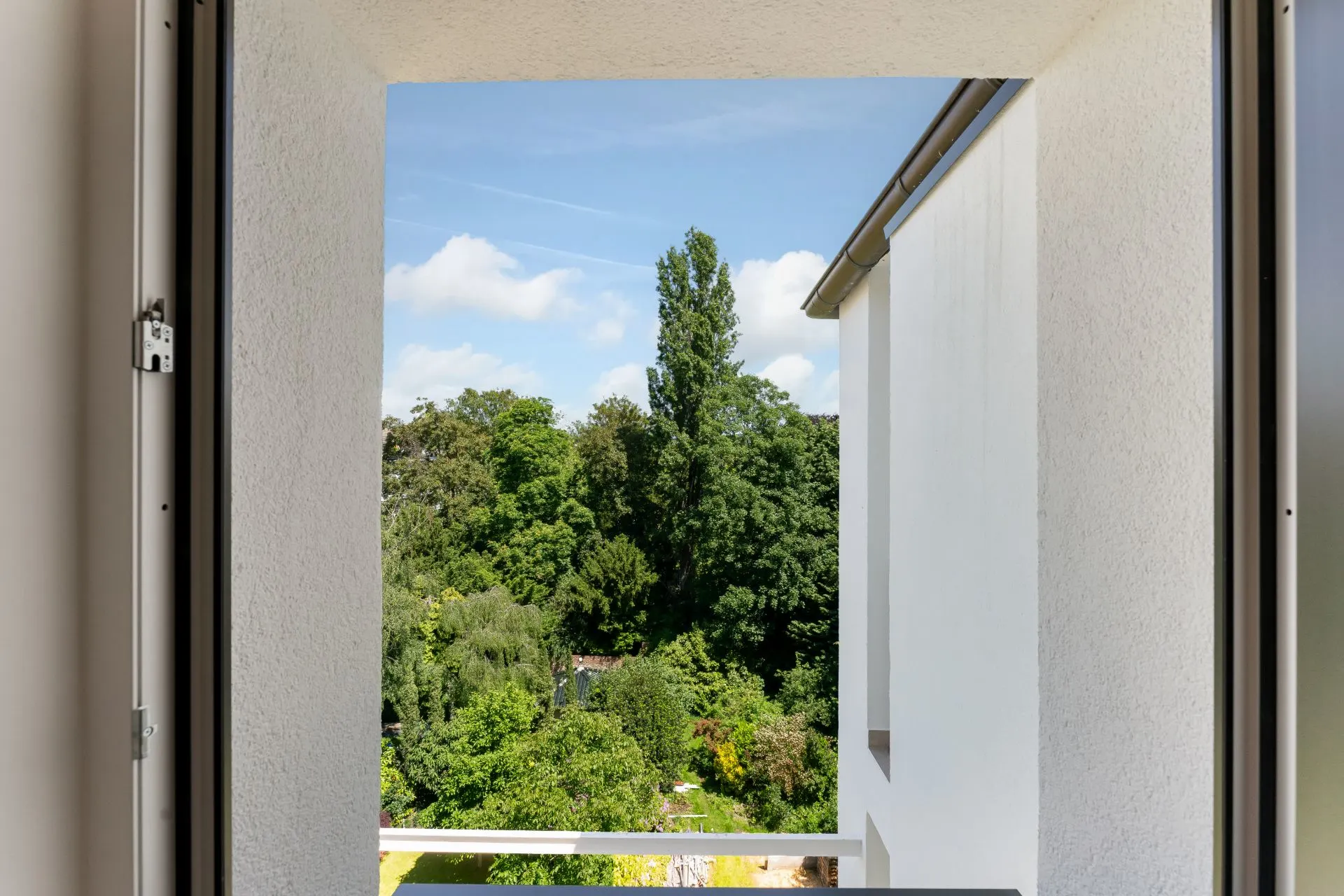Blick von einem Balkon auf grüne Bäume und blauen Himmel.