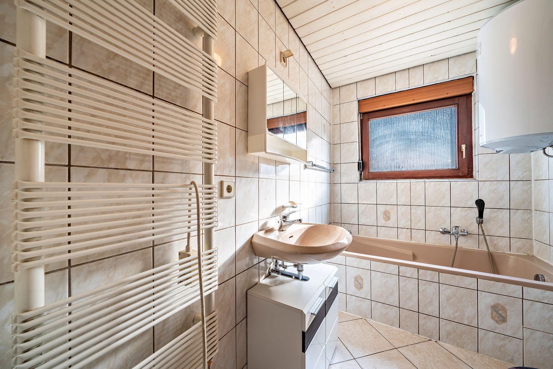 Badezimmer mit Waschbecken, Badewanne, Handtuchheizkörper und Fenster mit Holzrahmen.