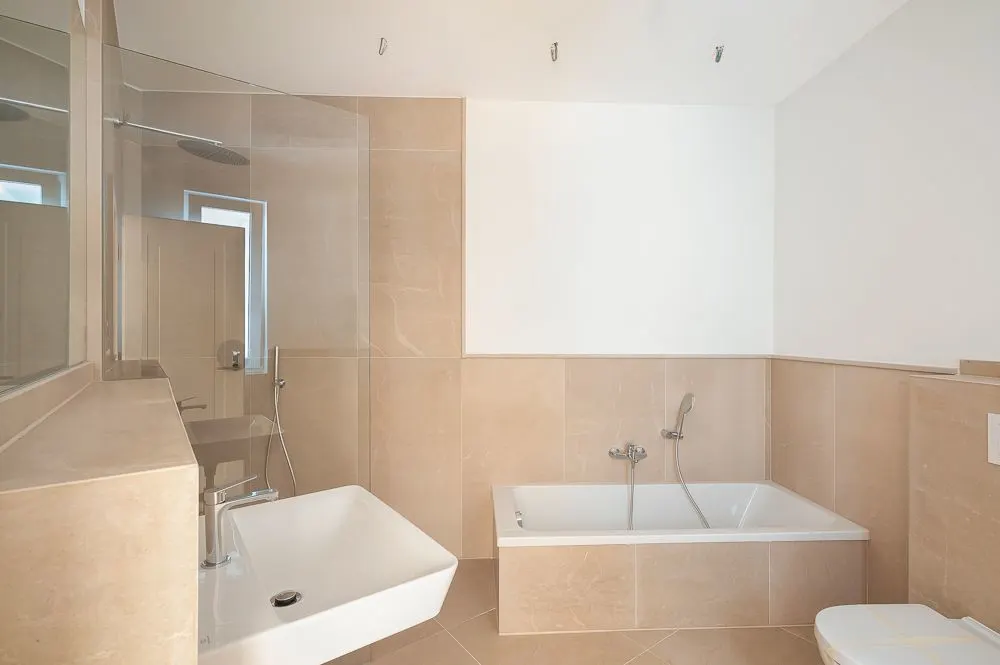 Helles Badezimmer mit Badewanne, Waschbecken, Dusche und WC, beige gefliest.