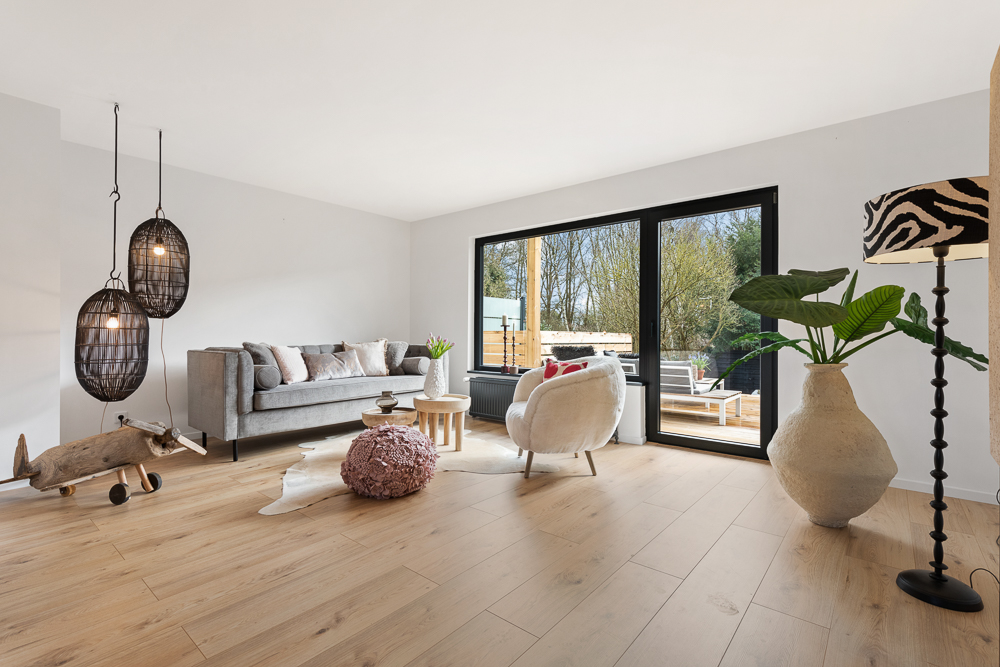 Modernes Wohnzimmer mit Sofa, Sessel, großen Fenstern und Holzboden.
