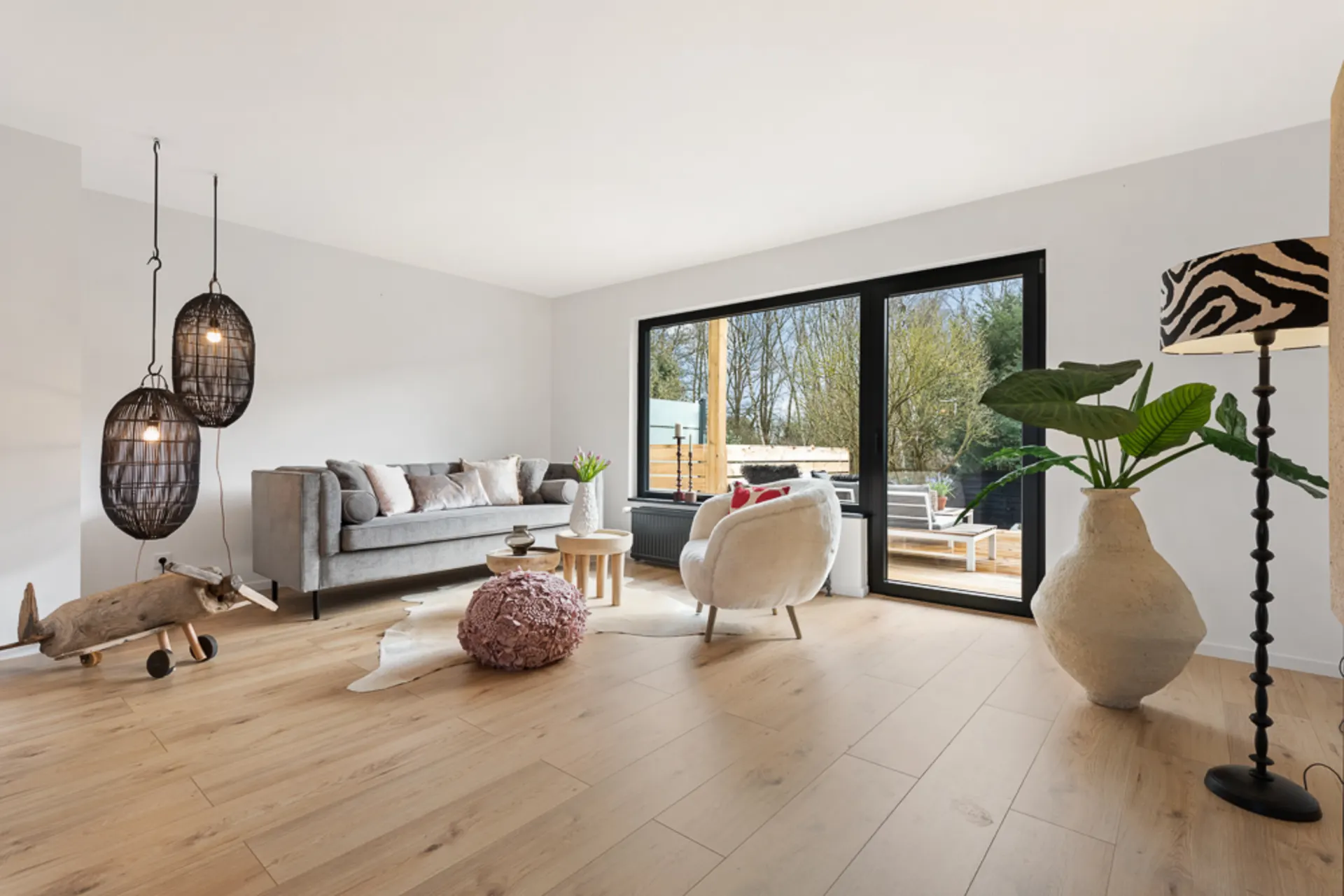 Modernes Wohnzimmer mit Sofa, Sessel, großen Fenstern und Holzboden.