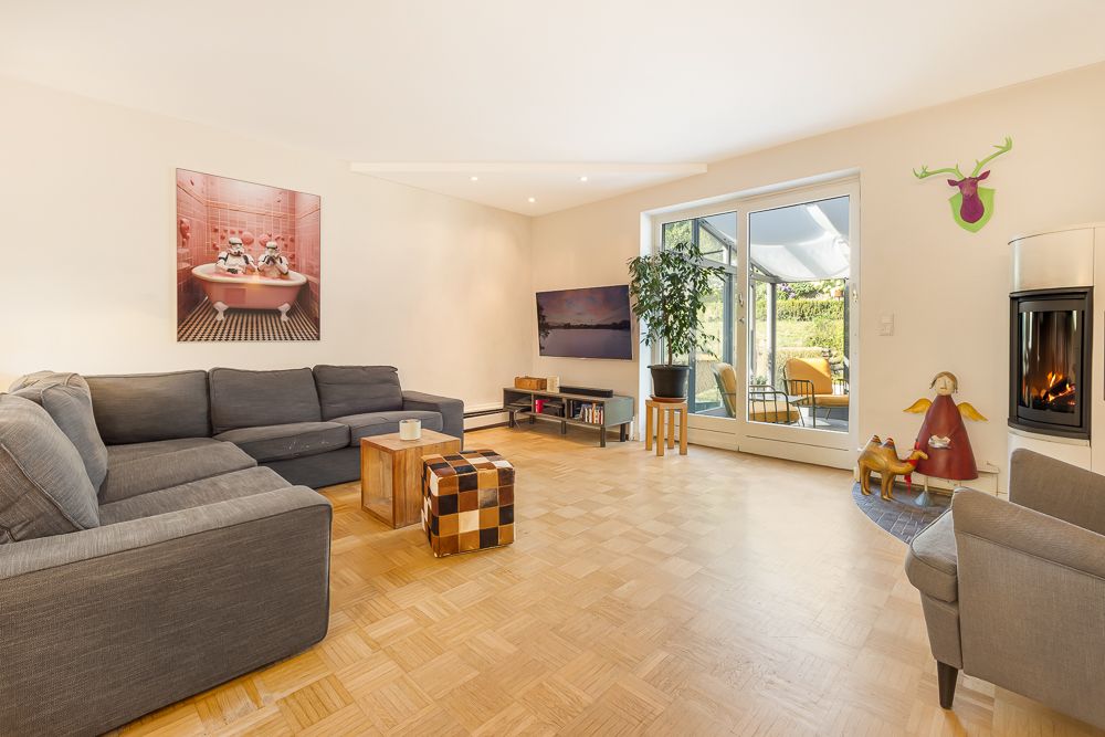 Modernes Wohnzimmer mit grauem Ecksofa, Fernseher, Kamin und Zugang zur Terrasse.