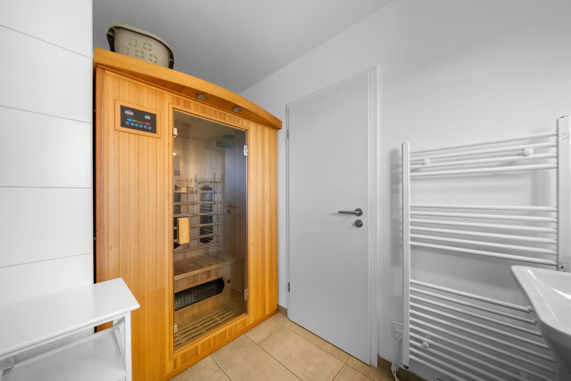 Kleiner Raum mit Infrarot-Sauna, weißer Tür und Handtuchheizkörper.