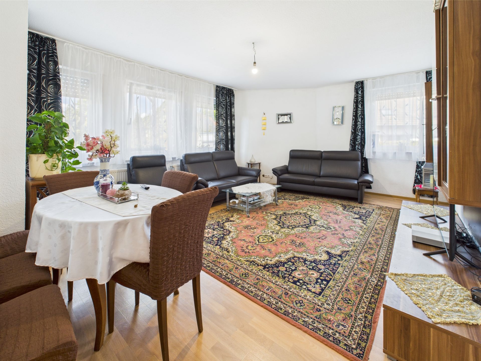Helles Wohnzimmer mit Teppich, zwei Sofas, Esstisch, Stühlen und großen Fenstern.
