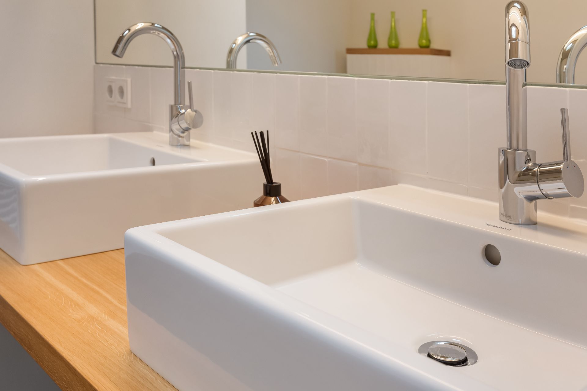 Zwei moderne Waschbecken mit Armaturen auf einer Holzplatte, Spiegel im Hintergrund.