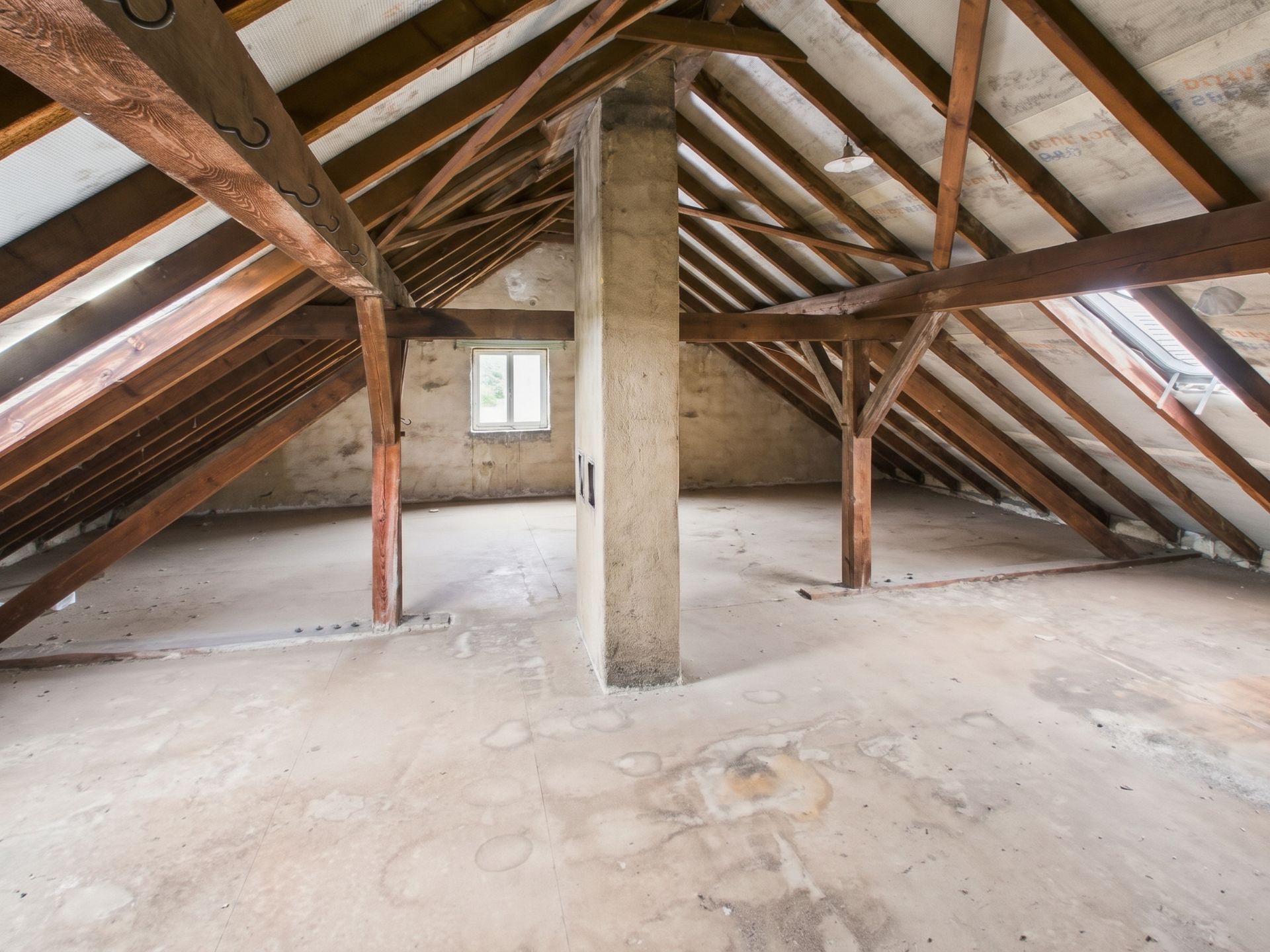 Leerer Dachboden mit Holzbalken und einem Fenster an der Stirnwand.