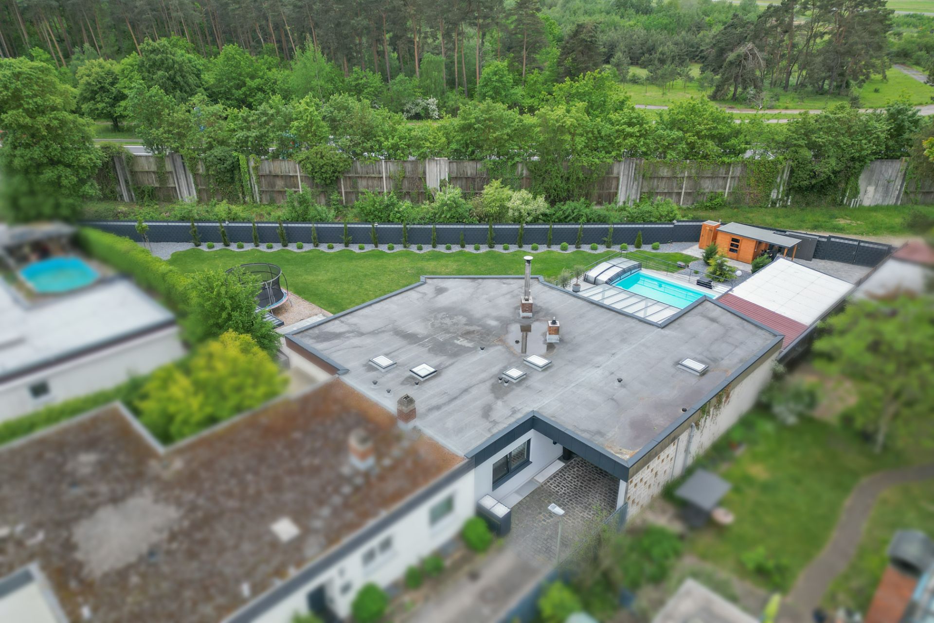Luftaufnahme eines Hauses mit Flachdach, Garten und überdachtem Pool im Hinterhof.