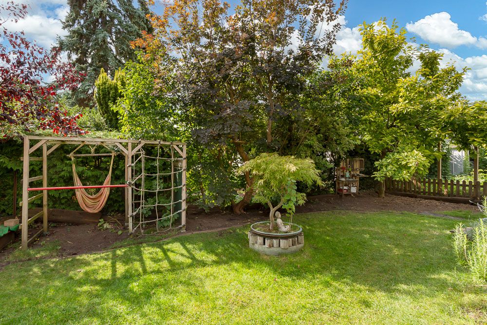 Garten mit Rasen, Bäumen, einer Hängematte im Holzgestell und kleinem Baum im Rundbeet.