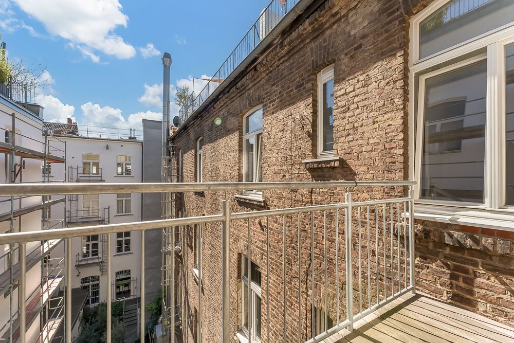 Balkon mit Metallgeländer an einem Backsteinhaus, Blick auf Innenhof und Nachbargebäude.