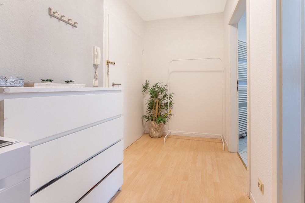 Heller Flur mit weißer Kommode, Pflanzen und leerem Kleiderständer auf Holzfußboden.