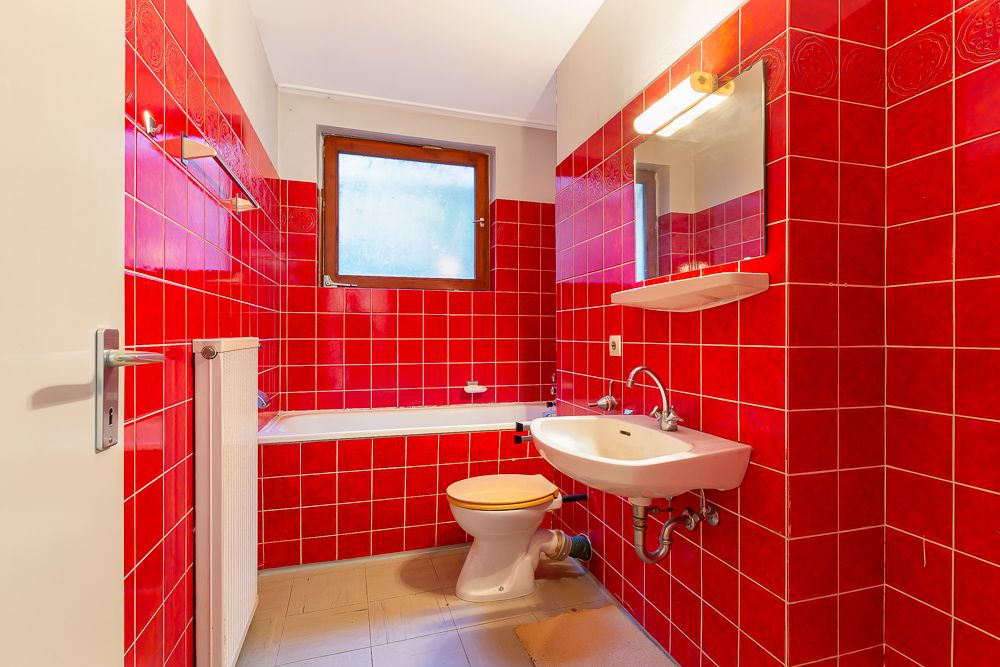 Badezimmer mit roten Fliesen, Waschbecken, Toilette, Badewanne und Fenster.