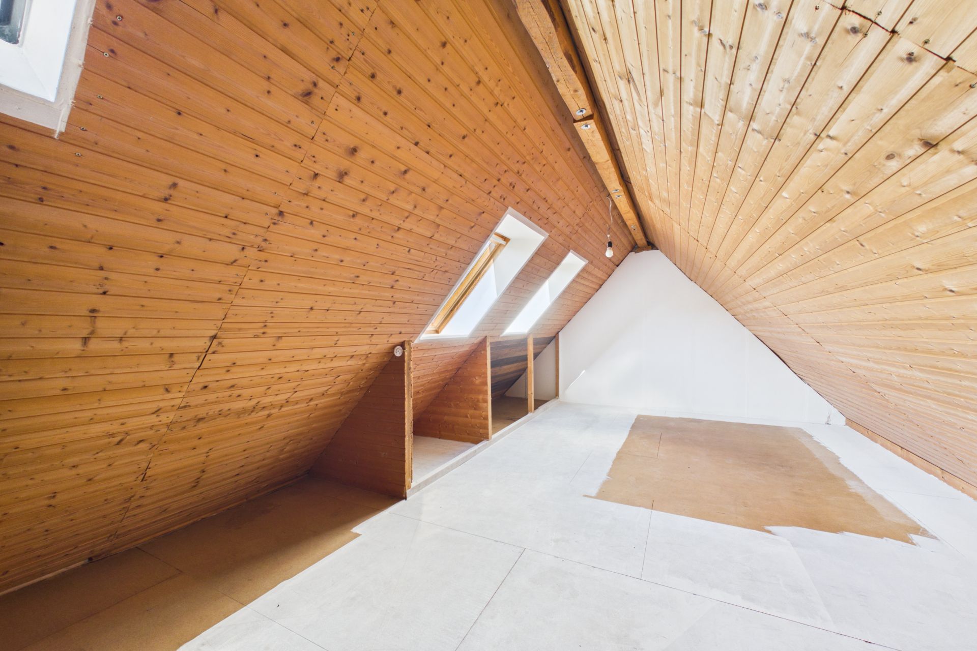 Dachbodenraum mit schräger Holzdecke und mehreren Dachfenstern, teils mit Teppichboden.