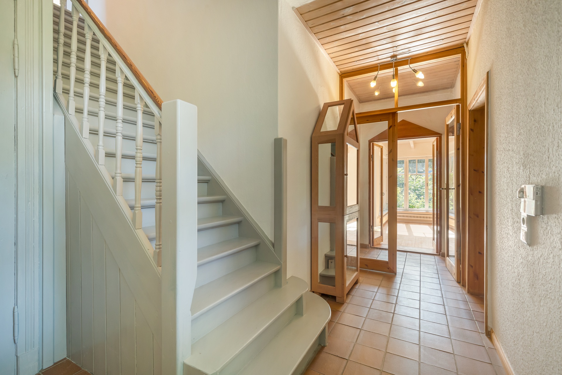 Heller Flur mit Treppe, Spiegel, Fliesenboden und Glastür am Ende.