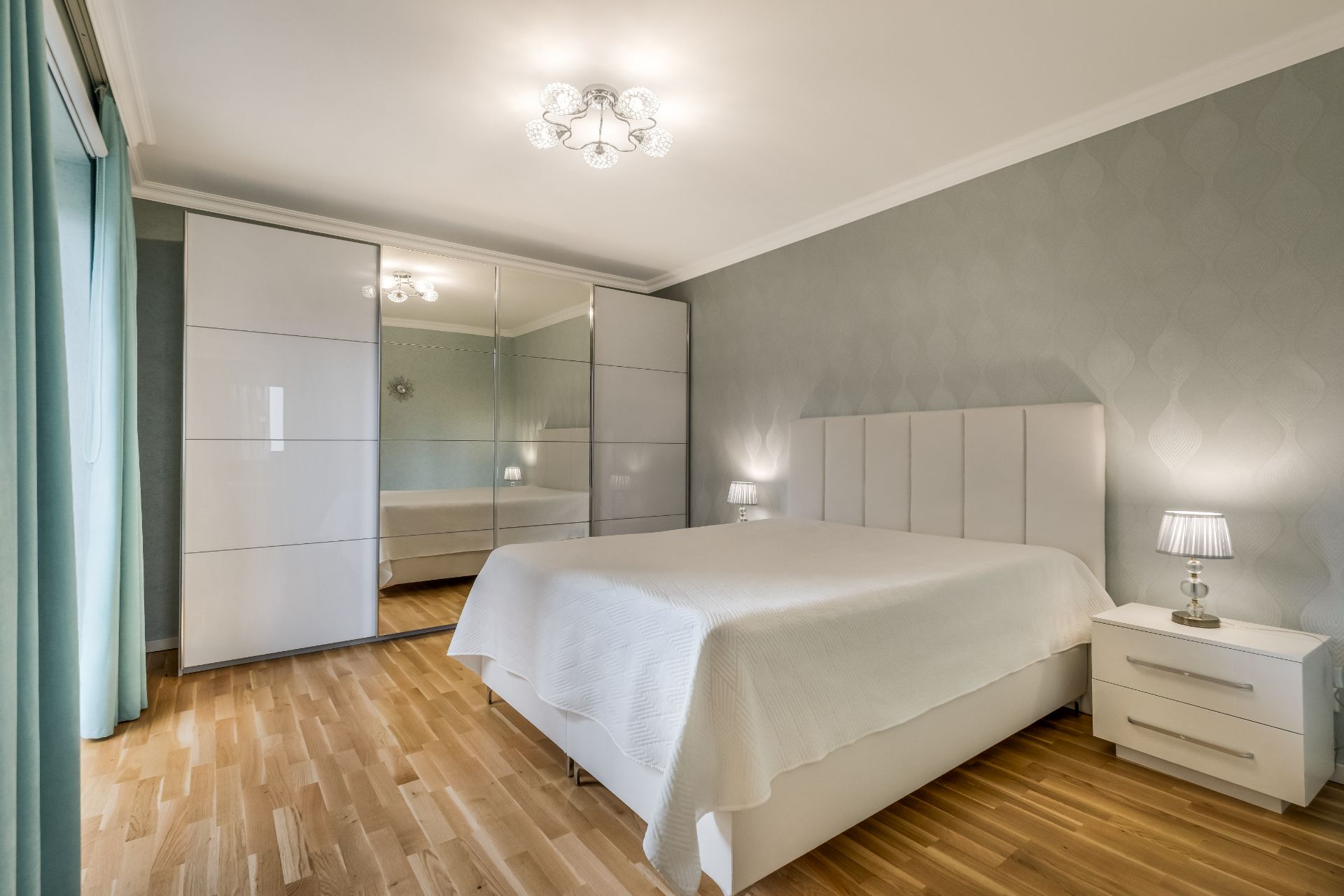 Modernes Schlafzimmer mit großem Bett, Nachttischen, Kleiderschrank mit Spiegeltüren und Holzfußboden.